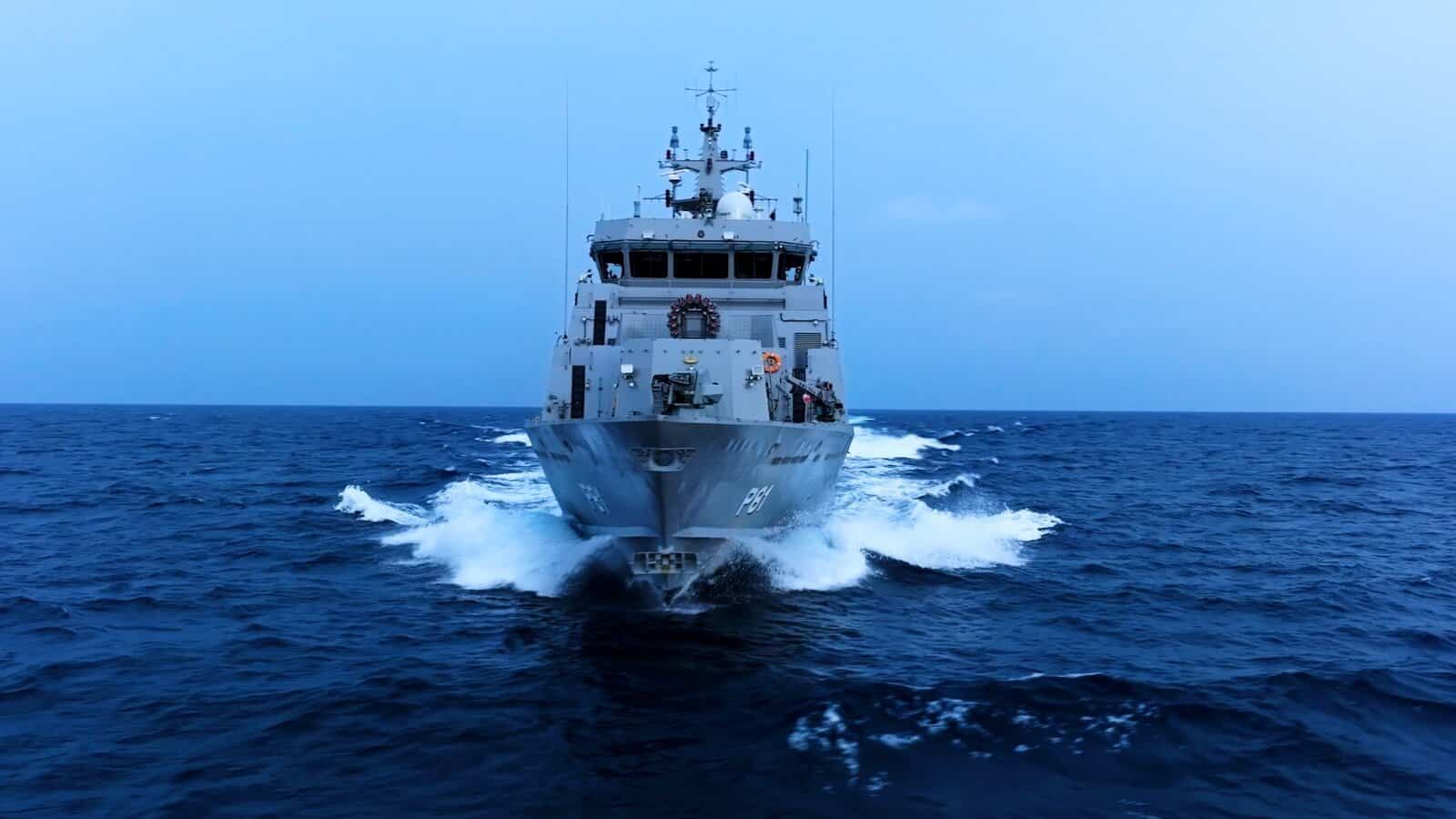 Military ship sailing on the ocean during daytime, with a clear blue sky.