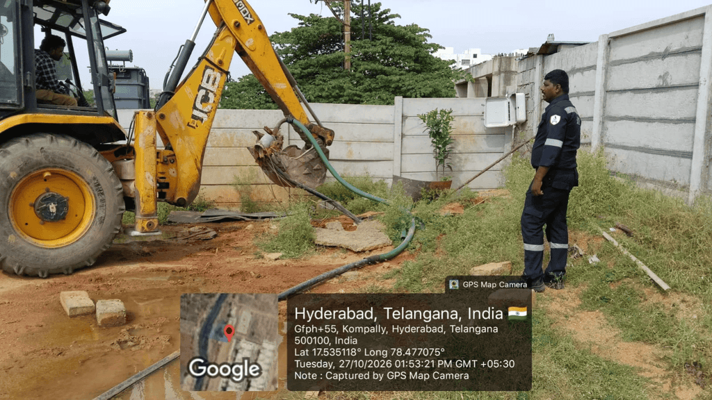 Excavator and officer at a site near a concrete wall, handling hoses and equipment in Hyderabad, India.