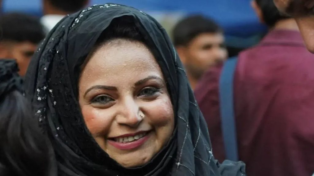Smiling woman wearing a black hijab in a crowd.