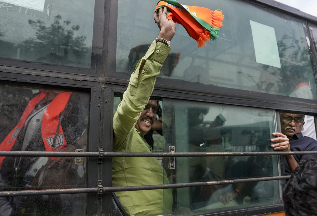 Man on a bus holding a saffron scarf with a smile, crowd around window.