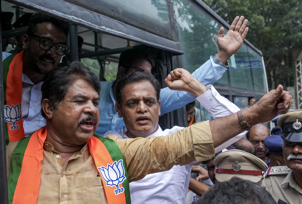 Politician raising arm while crowd and security present during political rally, BJP saffron scarves and a.