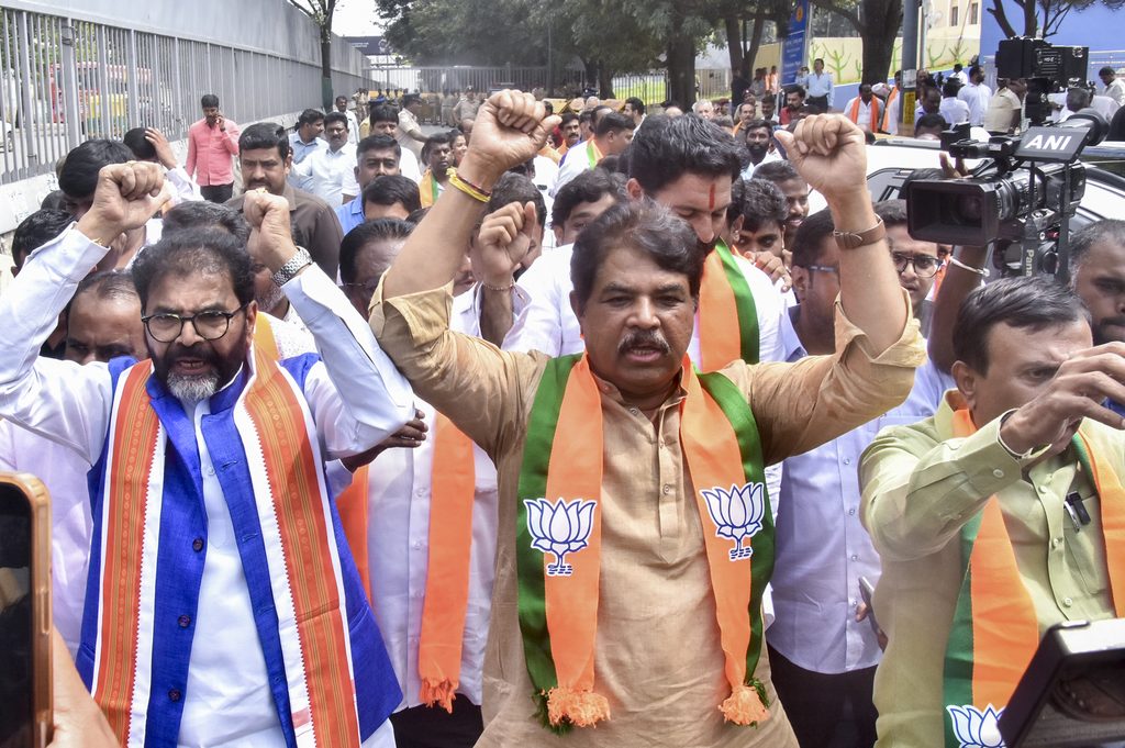 Political rally with BJP supporters raising fists, wearing saffron and green scarves.