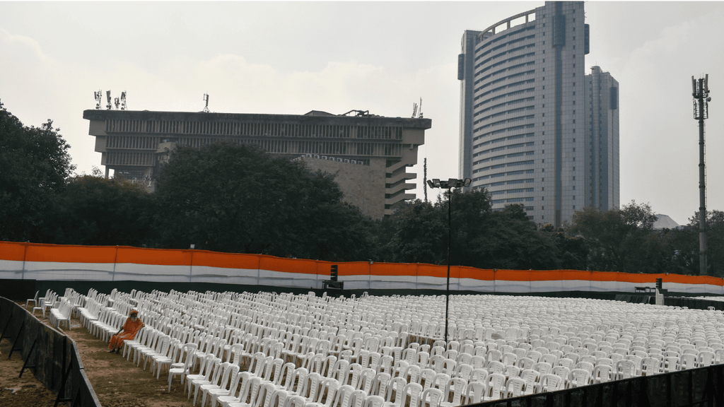 Rows of white chairs arranged for a public rally with tall buildings in the background.