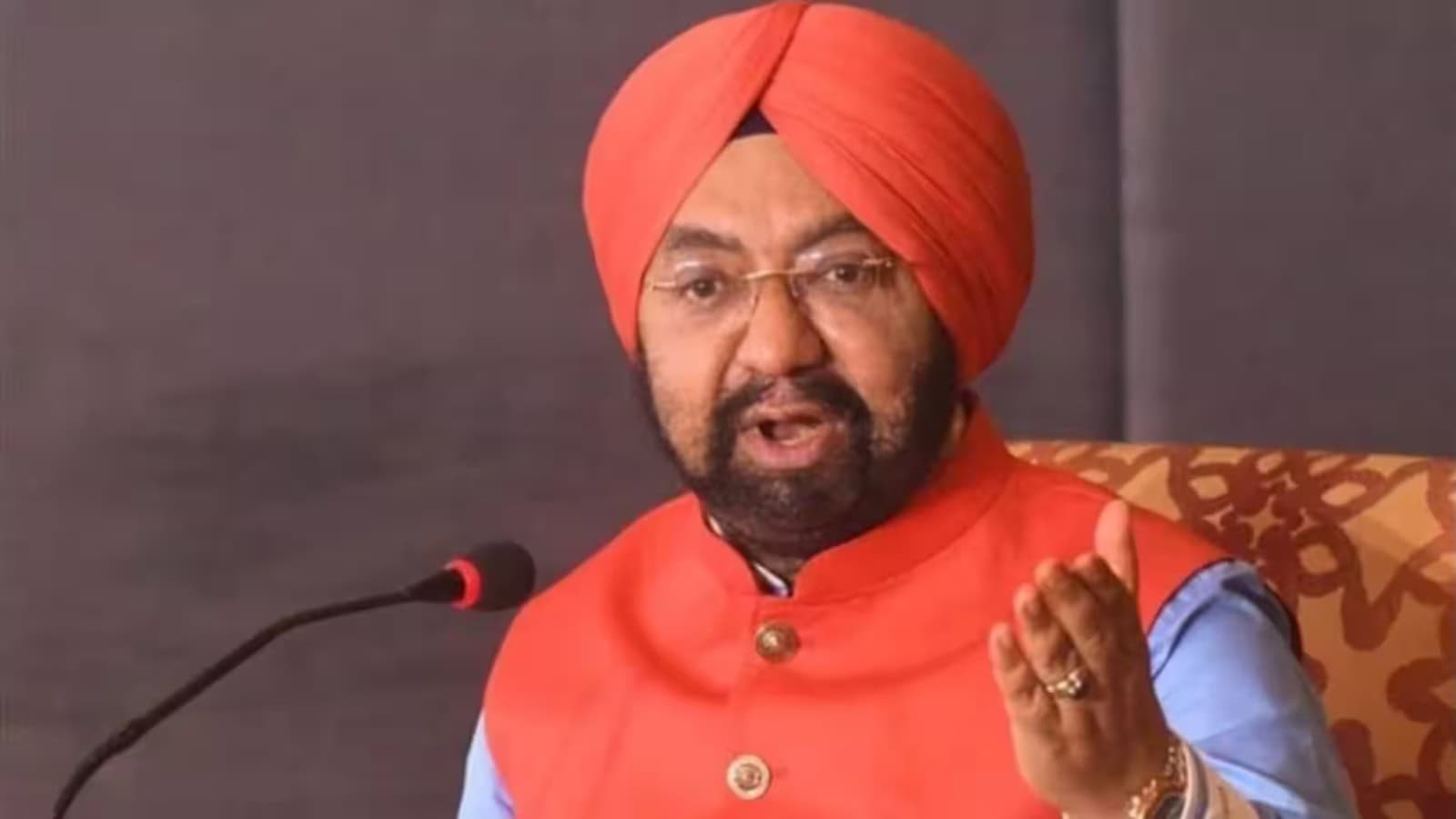 Vikramjit Singh Sahney wearing an orange turban and kurta speaking at a microphone.