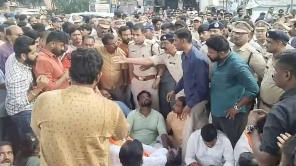 Crowd gathers around a seated man on the street amid police and onlookers during a public incident.