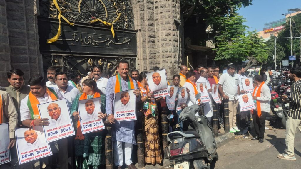 Protesters with posters at a Hyderabad rally, crowd gathered outside a historic gate.