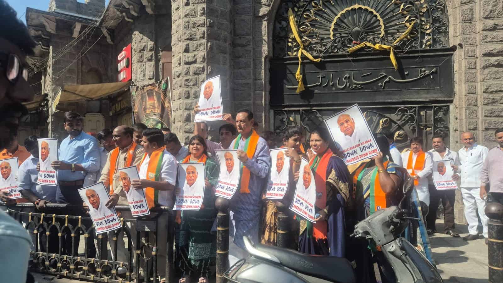Protesters outside a historic gate hold posters and wear orange sashes in Hyderabad demonstration.