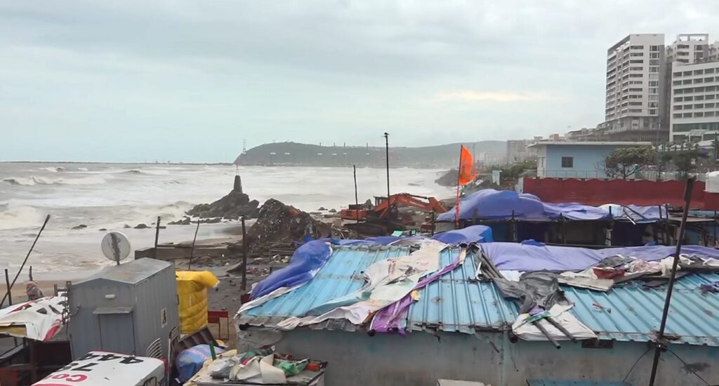 Severe cyclone aftermath along Andhra coast with damaged roofs and debris near the shoreline.