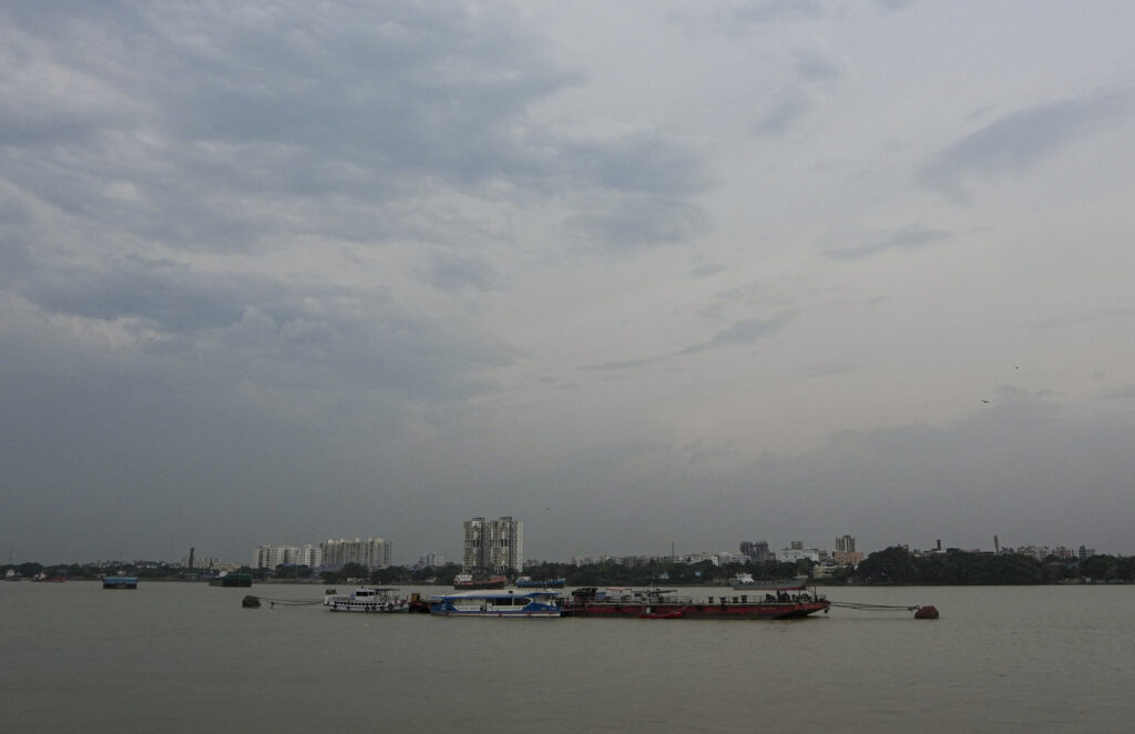 Silhouetted skyline and boats on a calm river under a cloudy sky.