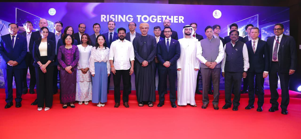 Group of diverse officials and leaders standing on a red carpet at a conference, in front of a purple 'R1.