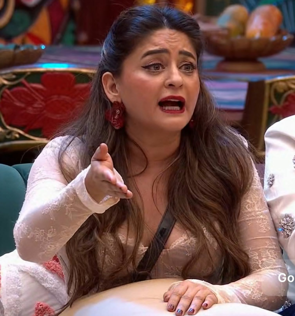 The Bigg Boss 20 contestant sits outdoors with a mug, wearing a white shirt and headband.