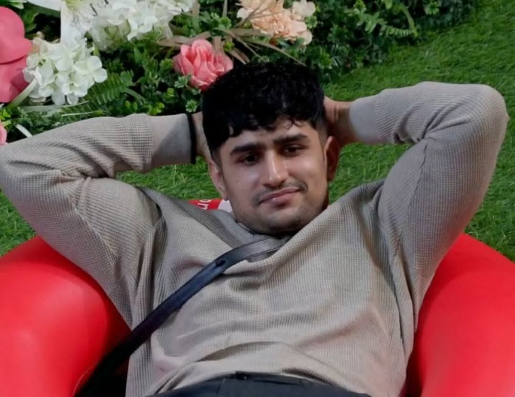 Young man relaxing on a red seat outdoors with greenery and flowers in the background.