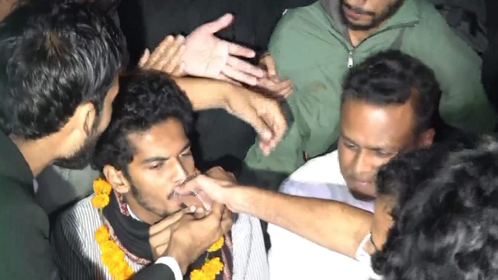 Group of men in a crowded setting with one man being restrained by others.